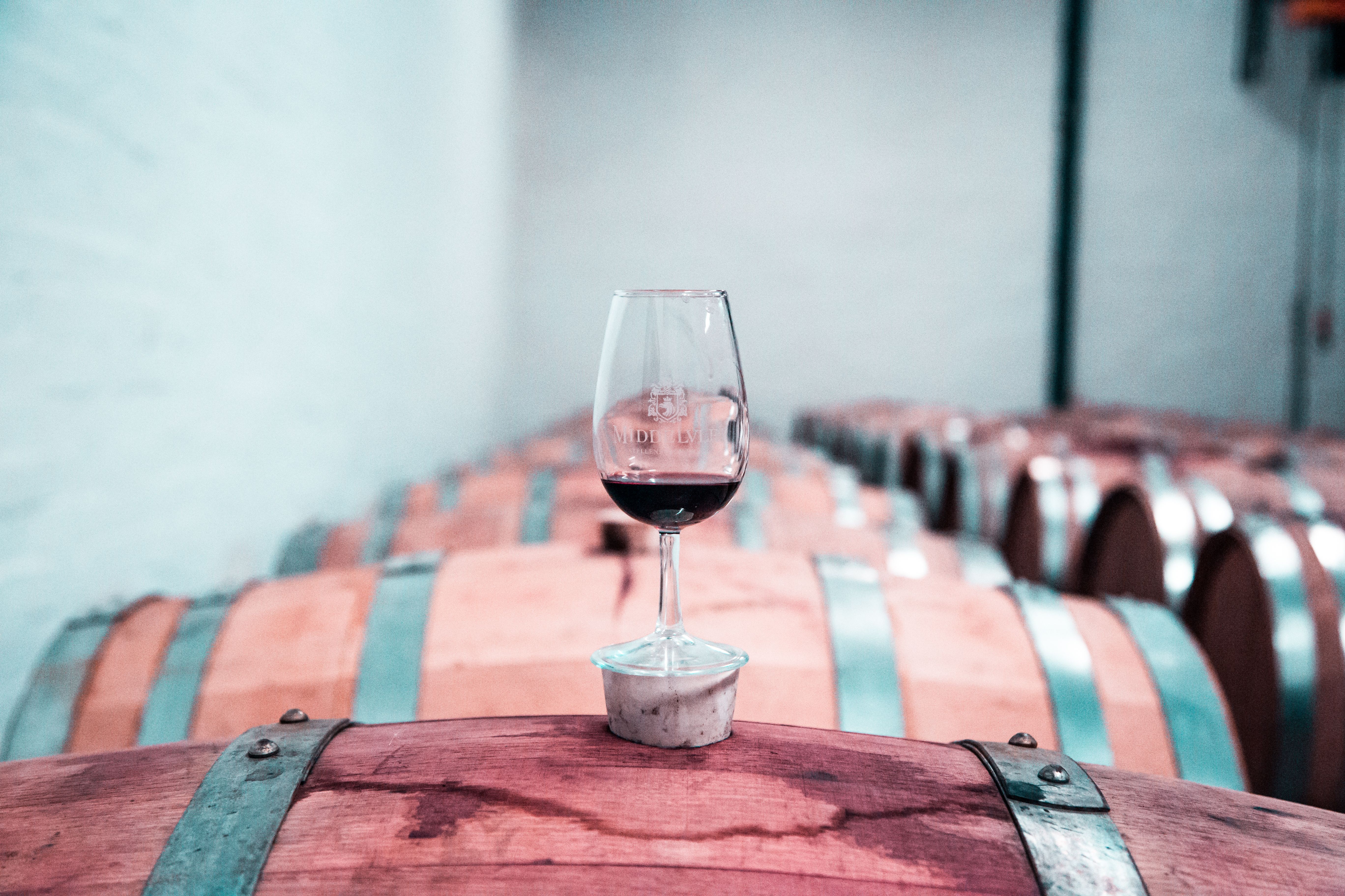 Ett glas rött vin står på en träfat i en vinkällare.