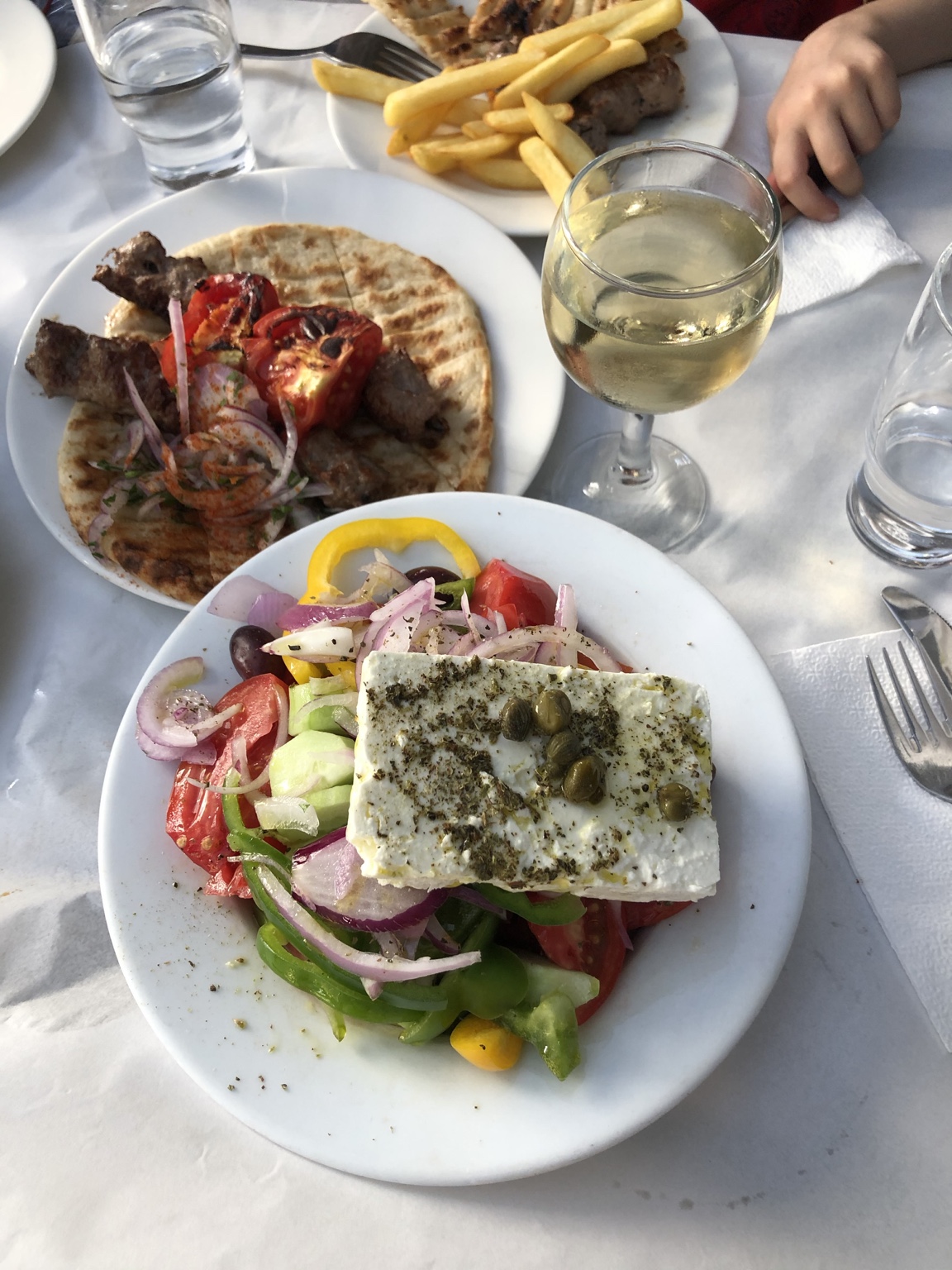 Grekisk sallad med feta, tomat, gurka, paprika, rödlök, oliver och kapris, med pitabröd på en tallrik bakom.