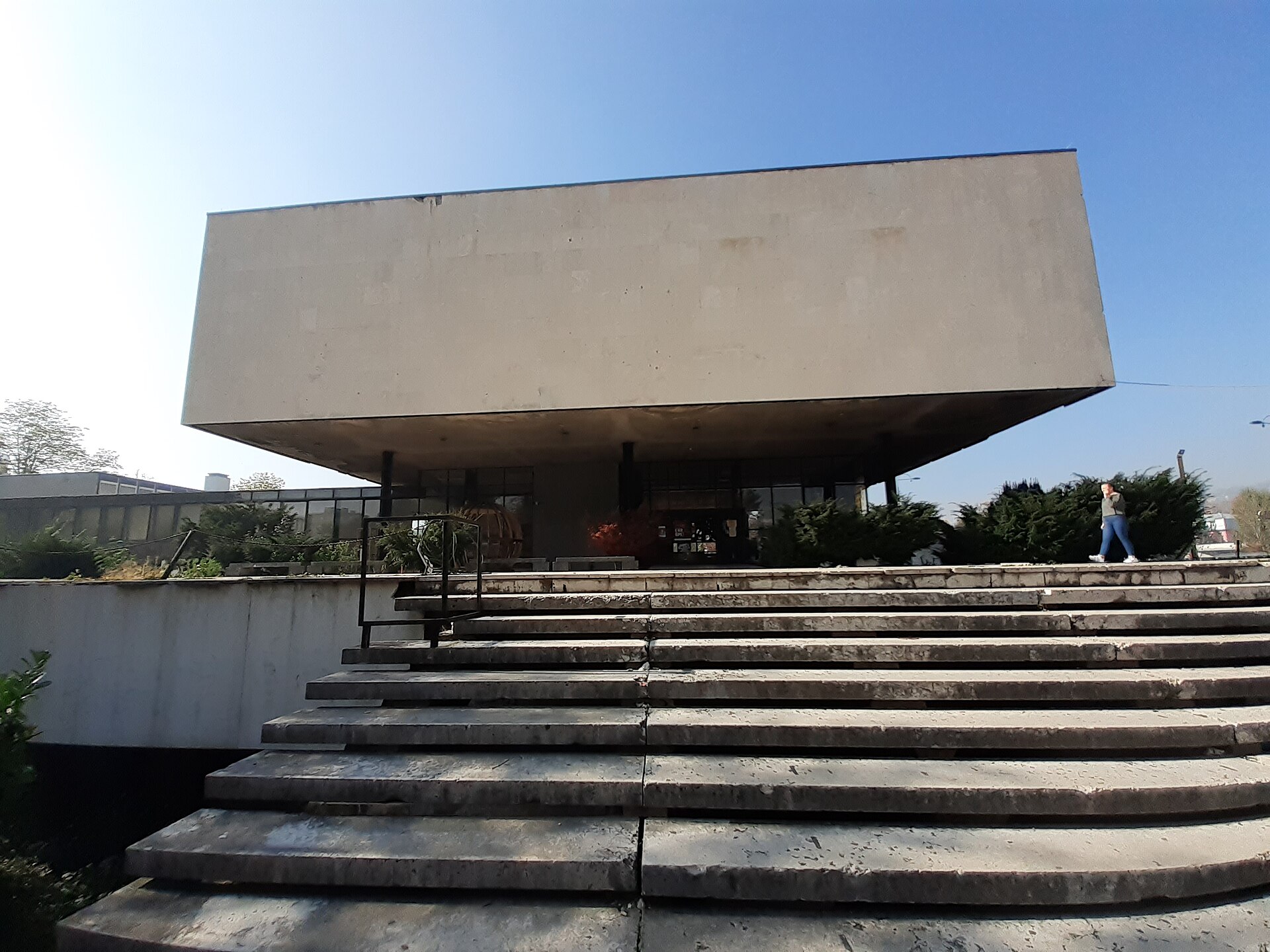 Breda betongtrappor leder upp mot den svävande, kubformade betongbyggnaden som utgör Historiska museet i Sarajevo.