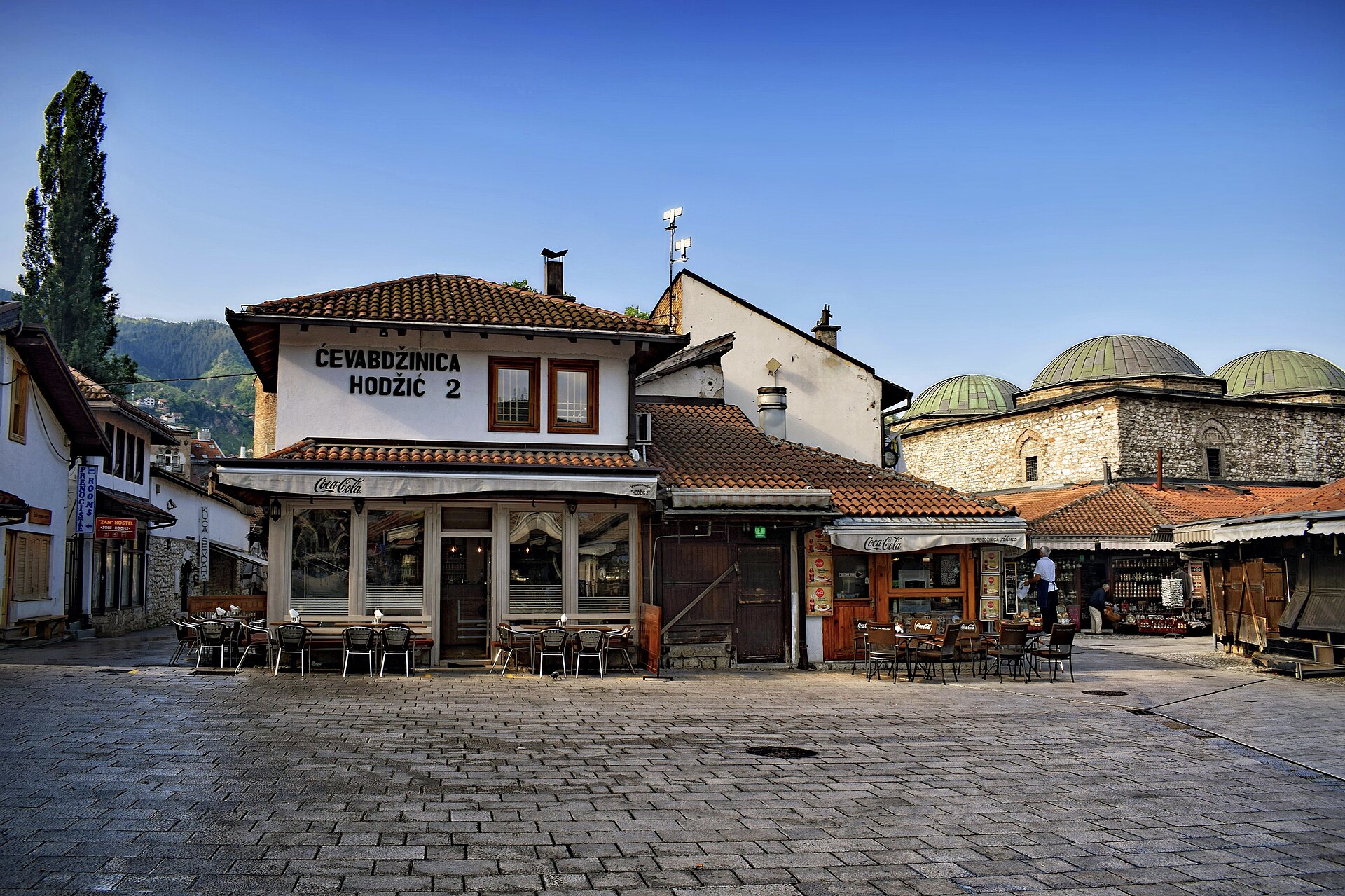 Ćevabdžinica Hodžić i Baščaršija i Sarajevo, med uteserveringens stolar på det tomma torget i morgonljuset.