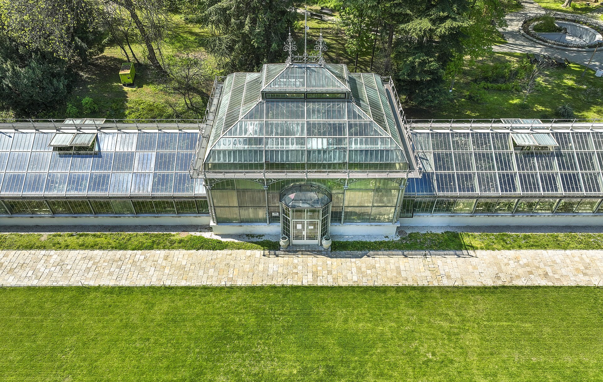 Ett vackert historiskt växthus i gjutjärn och glas omgivet av lummig grönska i Jevremovac botaniska trädgård i Belgrad.