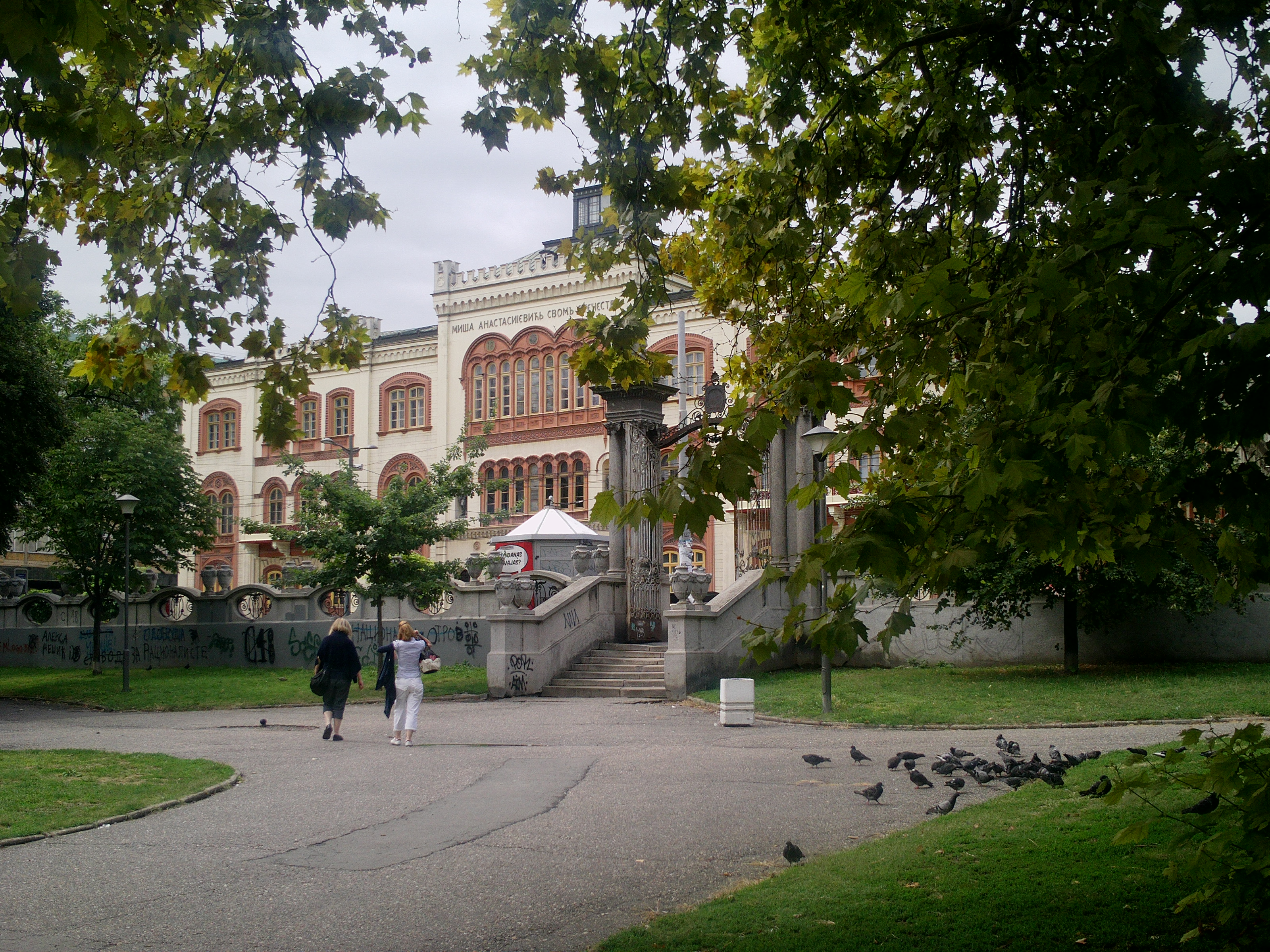 Belgrads universitets rektorat sett från Studentparken, en gul nyklassicistisk byggnad bakom höga träd.