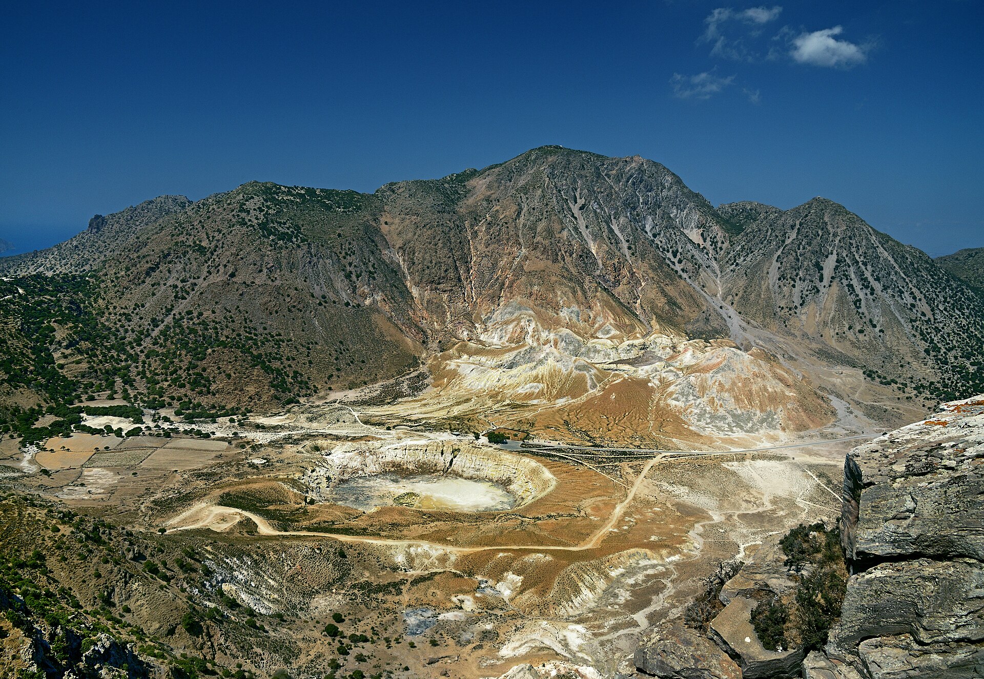 En vidsträckt vy över den runda Stefanoskratern i vulkankalderan på Nisyros, fotograferad från bergsbyn Nikia under en blå himmel.