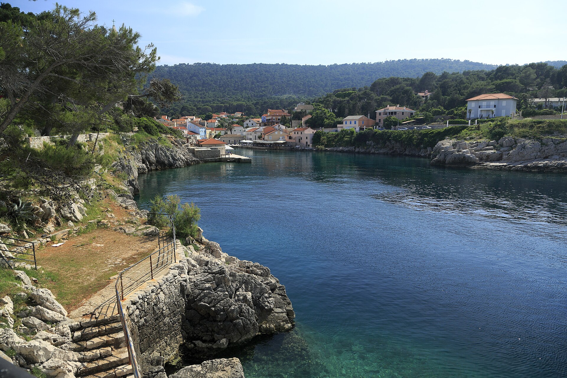 En naturskön vik på ön Lošinj i Kroatien med kristallklart turkost vatten omgivet av gröna tallar och klippor.