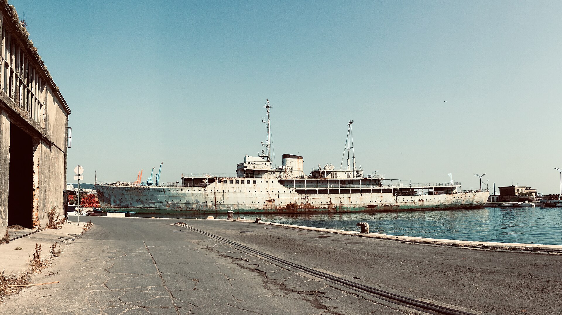 Det rostiga historiska fartyget Galeb ligger förtöjt vid en betongkaj i Rijekas hamn under en klarblå himmel.