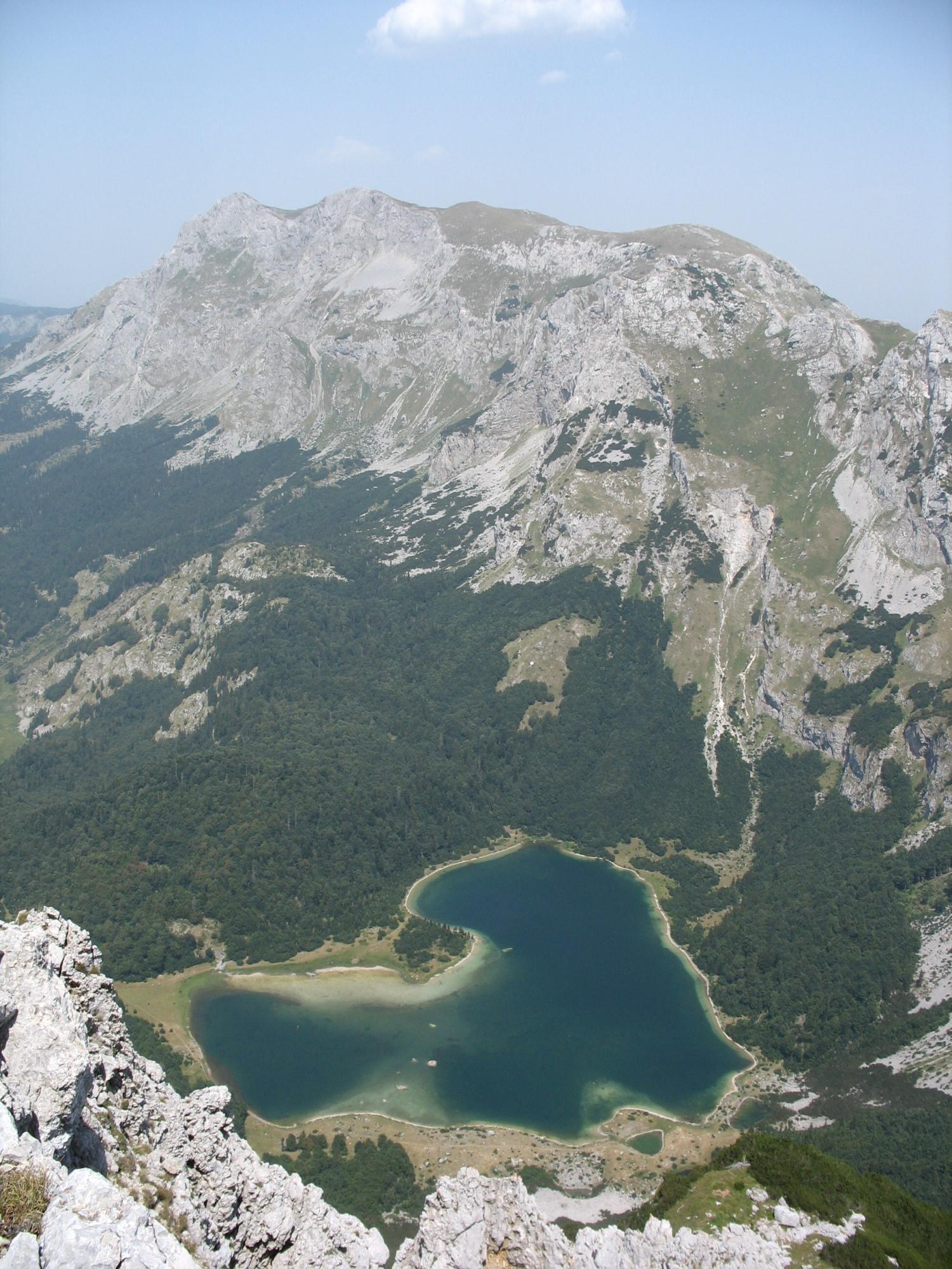 Vy över den hjärtformade sjön Trnovačko jezero omgiven av dramatiska bergstoppar och gröna sluttningar i Sutjeska nationalpark.