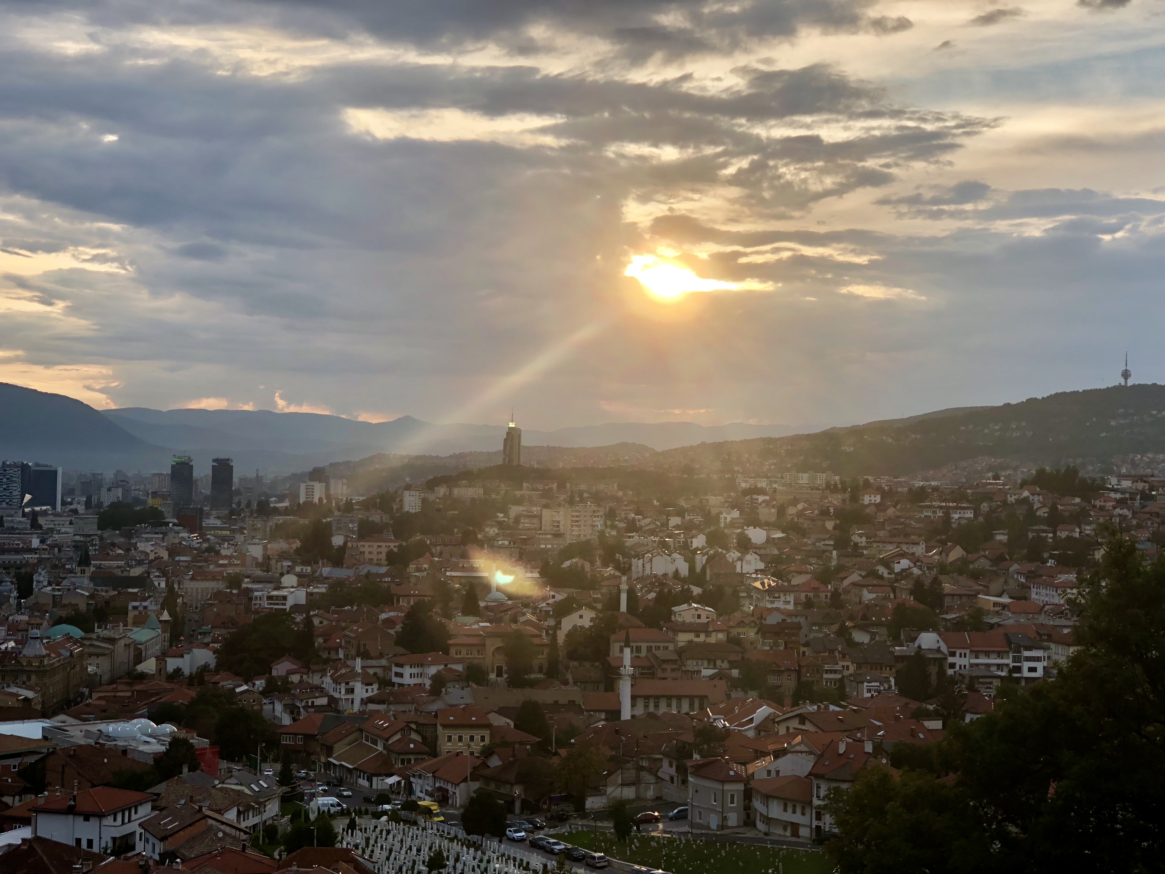 Utsikt över Sarajevo i solnedgång med stadens tak, minareter och omgivande berg.