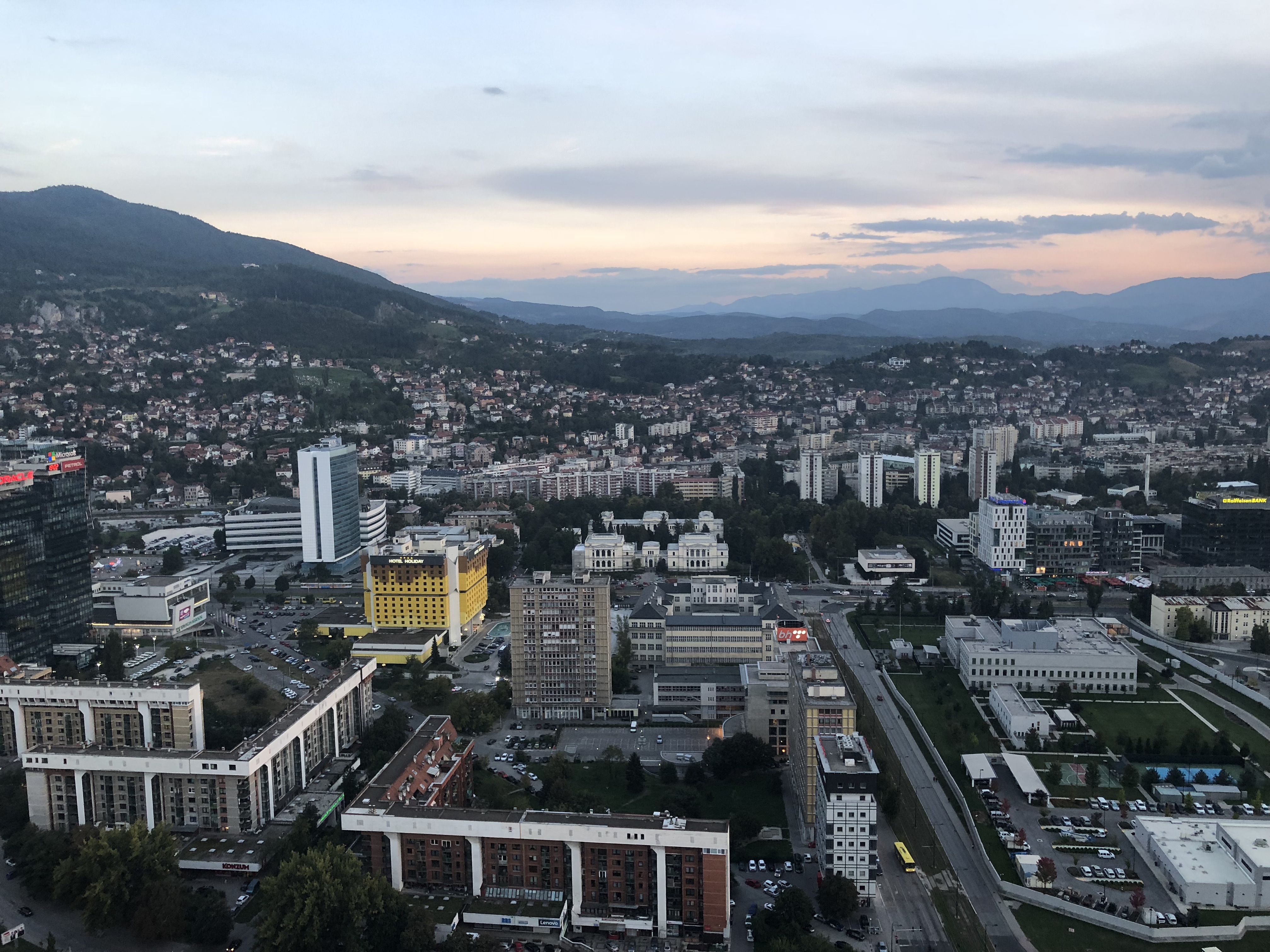 Panoramavy över moderna delar av Sarajevo med höghus, bostadskvarter och berg i bakgrunden.