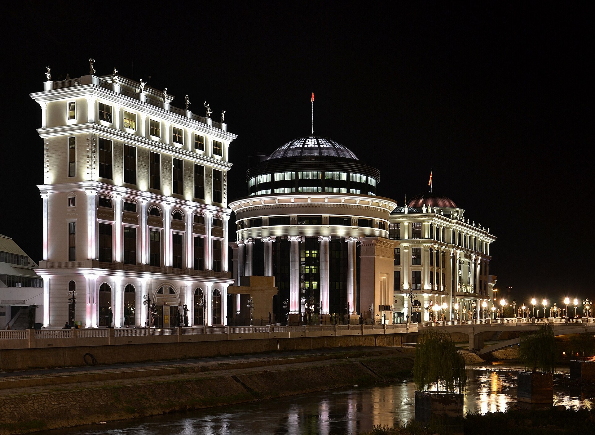 Upplysta nyklassicistiska byggnader längs floden Vardar i Skopje under natten, en del av det kontroversiella Skopje 2014-projektet.
