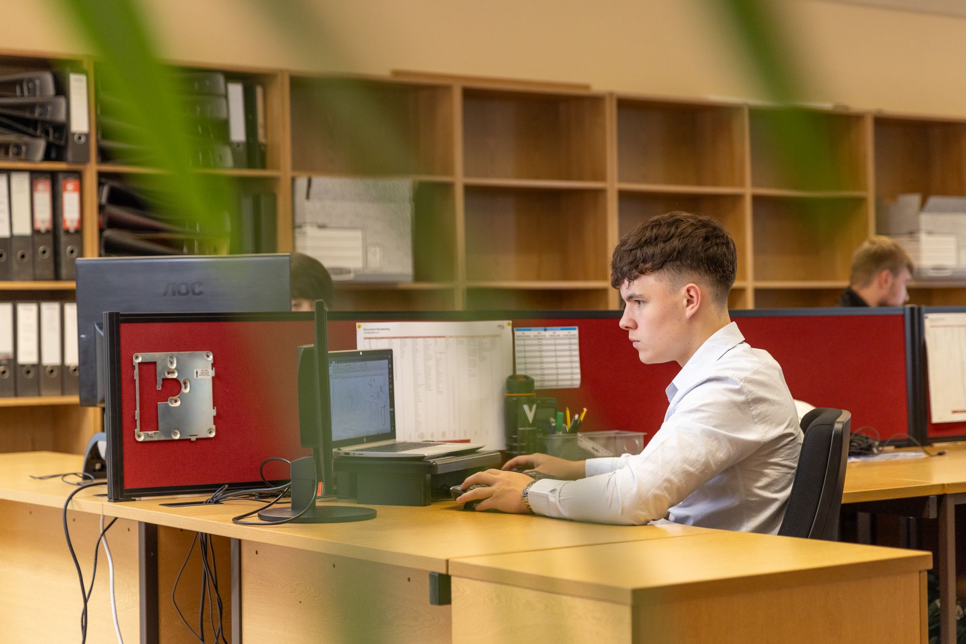 En ung man sitter djupt fokuserad framför en datorskärm i en modern kontorsmiljö.