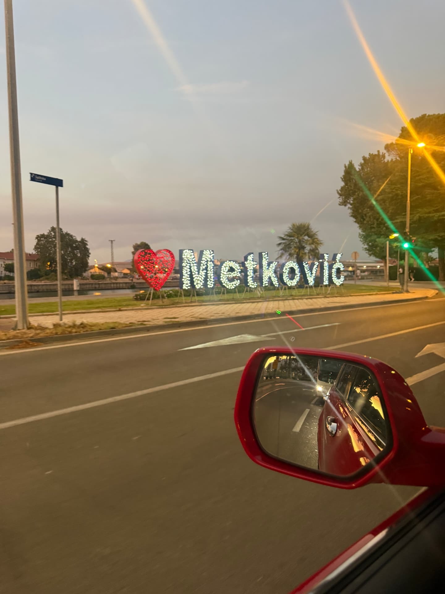 Den upplysta Metković-skylten sedd från bilen i kvällsljus.
